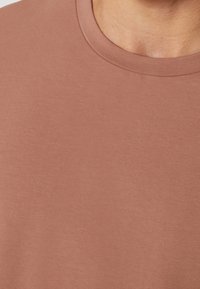 Krótki rękaw, okrągły dekolt t-shirt w miękkim, stonowanym kolorze terakoty o gładkiej fakturze i minimalnych szwach.