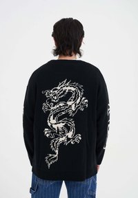 Czarny sweter dzianinowy z dużym białym wzorem smoka na plecach oraz skomplikowanymi wzorami na rękawach. Teksturowany materiał, okrągły dekolt.