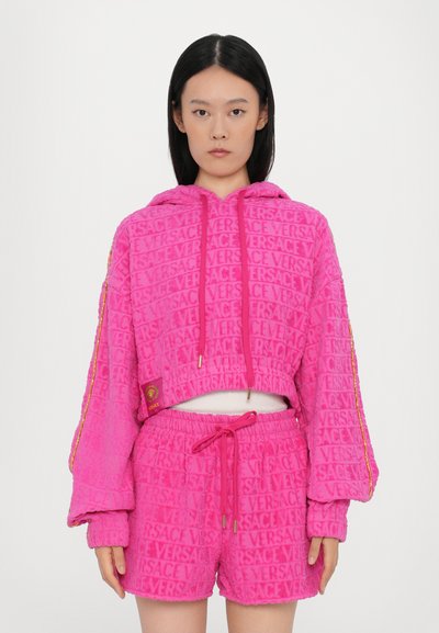 Ensemble de sweat à capuche court rose et de shorts, avec un tissu texturé, un motif logo en tout sur l'ensemble, une fermeture à cordon de serrage et des détails en accent doré.