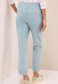 Pantalons bleu clair avec une taille élastique et des chevilles resserrées, dotés de deux poches arrière et d'une texture douce et lisse.