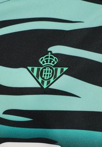 Ljusblå och svart mönstrad tyg med en triangulär logotyp med en krona och initialerna "DB" i en präglad design.