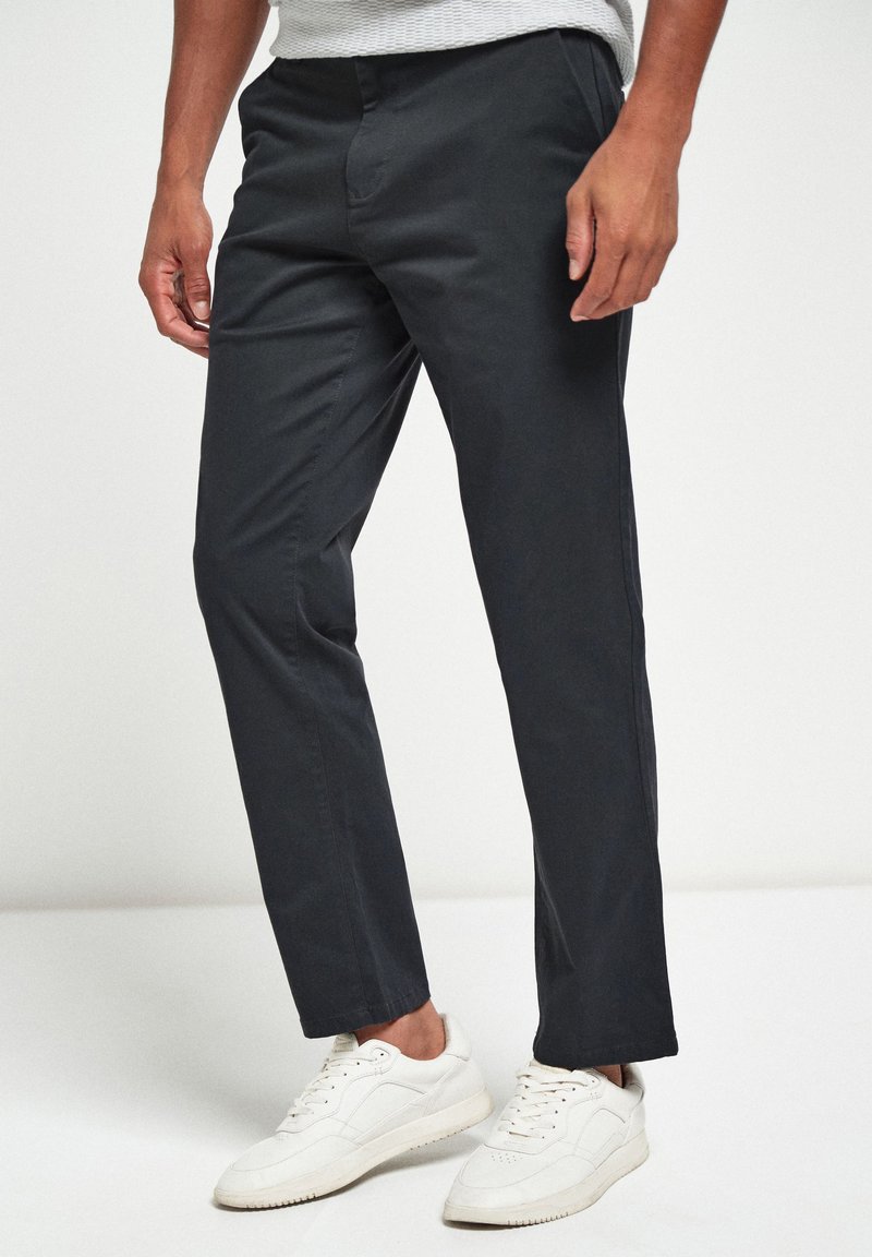 Pantalones elásticos de color gris oscuro con un corte slim, que presentan una textura suave y una parte frontal plana. Combinados con zapatillas blancas.