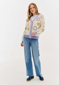 Pletený cardigan ve krémové barvě s vzory srdcí v růžové, žluté a fialové. Má výstřih do V, zapínání na knoflíky a kontrastní žebrované manžety a lem.