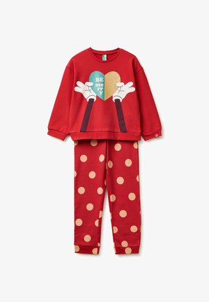 Felpa rossa con mani stampate che tengono un cuore turchese e dorato, abbinata a pantaloni rossi con grandi pois beige.