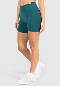 Teal fitted shorts van rekbaar materiaal, met een hoge tailleband en omgeslagen pijpen. Gecombineerd met witte sport schoenen en enkelsokken.
