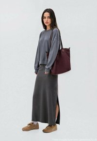 Sivi dukserica, tamnosiva maxi suknja s bočnim prorezom, bež tenisice i burgundska torba. Glatka tkanina s opuštenim dizajnom.