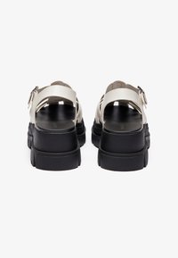 Light beige platform sandals with black rubber soles, featuring an adjustable ankle strap and a textured upper for grip.