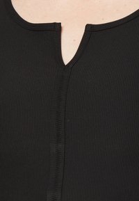 Haut noir côtelé avec un décolleté en V et un détail de couture centrale. Le tissu a une texture lisse.