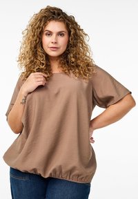 Brown, short-sleeve top with a loose fit and gathered hem. Fabric has a textured finish. Paired with blue jeans.