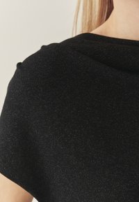 Sort striktop med en blød tekstur, løst fit og en subtil glans. Designet inkluderer en draperet halsudskæring og afslappede ærmer.