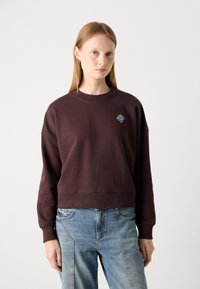 Sudadera corta marrón con cuello redondo y puños acanalados, que presenta un pequeño logo bordado en azul claro en el pecho.