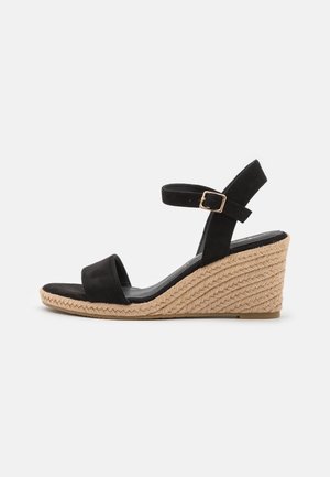 Zwarte suède wedge sandaal met enkelband en gouden gesp, gevlochten jute platformzool voor casual zomerkleding.