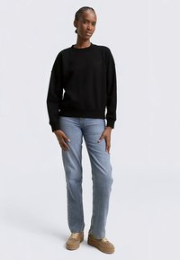 Felpa nera con scollo rotondo, polsini e orlo a coste. Abbinata a jeans blu chiaro a gamba dritta e sneakers platform color cuoio.