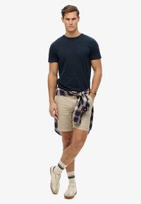 Marines T-shirt, beige shorts, ternet skjorte bundet om taljen, hvide sneakers med en beige sål, og mønstrede sokker med grønne striber.