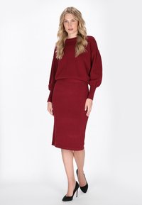 Set din pulover tricotat bordeaux și fustă midi, cu o croială lejeră, manșete ribbate și textură netedă, asortat cu tocuri negre.