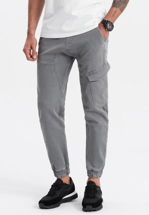 Pantalones cargo grises con puños elásticos, bolsillo lateral y textura desgastada. Combinados con zapatillas negras. Diseño simple y funcional.