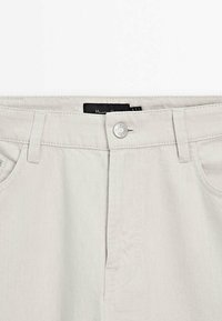 Pantalon en jean beige clair avec fermeture devant par bouton et zip, passants de ceinture et poches avant.