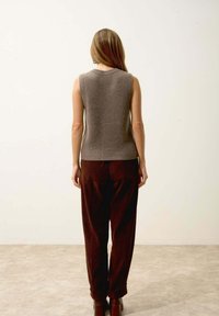Bezrukávý, proužkovaný šedý top v kombinaci s volnými hnědými kordovými kalhotami. Hnědé kotníkové boty dokončují outfit. Jednoduchý, neformální design.