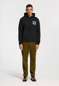 Black hooded sweatshirt with a front pocket and colorful floral graphic. Paired with olive green corduroy pants and black sneakers.