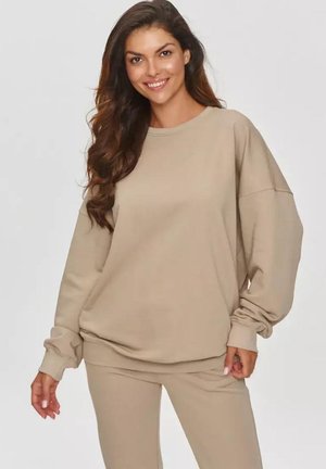 Beżowy, luźny sweatshirt z miękkiego materiału, okrągłym dekoltem i opadającymi ramionami, w komplecie z dopasowanymi spodniami, na jednolitym tle.