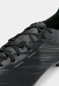 Μαύρο ποδοσφαιρικό παπούτσι με λεία δερμάτινη επάνω επιφάνεια, σχέδιο με κορδόνια και υφασμένα μαύρα στοιχεία. Διακριτική τριπλή ρίγα στο πλάι.