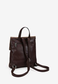 Mochila de cuero marrón con un acabado suave, que presenta un bolsillo delantero con cremallera, asas dobles para llevarla y un diseño superior estructurado.