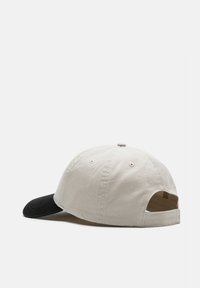 Cappellino bicolore con corona in cotone beige e visiera nera. Dotato di fori di ventilazione e cinturino regolabile sul retro.