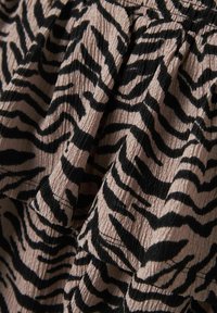 Un tissu noir et beige avec des volants et une texture froissée présente un motif audacieux de rayures zébrées. Un gros plan met en évidence le design.
