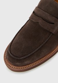 Dark brown suede loafer with stitched detailing and a leather sole, shown from a top-angle close-up.