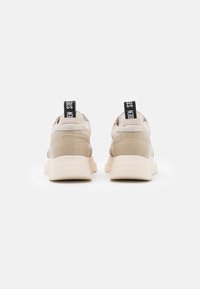 Sneaker beige con motivo in pelle di coccodrillo testurizzato sul retro. Presentano un colletto imbottito e un'etichetta di trazione con scritta nera. Suola spessa bianca.
