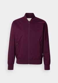 Burgundijas bomber jakas ar rāvējslēdzēju, elastīgiem piedurkņu galiem un apakšmalu. Iekļauj sānu kabatas un diskrētu logo uz krūtīm. Gluda auduma tekstūra.