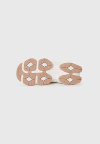 Semelle de chaussure avec un schéma de couleurs beige et blanc cassé, dotée de motifs de traction en caoutchouc et d'accents en forme de diamant pour une meilleure adhérence.