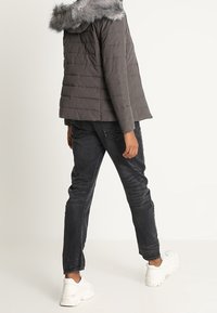 Polstret grå jakke med hætte af imiteret pels, kort design og lodret quiltning, kombineret med mørke jeans og hvide plateau-sneakers.