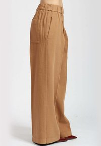 Pantaloni a gamba larga in tessuto beige, con vita alta elasticizzata, tasche laterali e una finitura liscia e testurizzata.