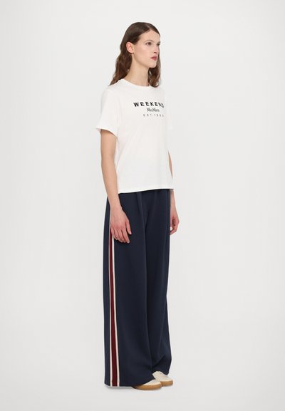Weißes, kurzes T-Shirt mit schwarzem Text "WEEKEND MaxMara EST.1983", kombiniert mit lockeren, marineblauen Hosen mit weißen und dunkelroten Seitenstreifen.