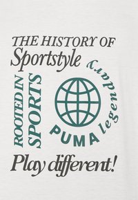 Witte stof met daarop bedrukte tekst in zwart en groen. De tekst bevat zinnen over sportstijl en een wereldbol graphic nabij "PUMA."