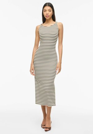 Mujer con vestido midi beige sin mangas con finas rayas horizontales negras, de pie frente a un fondo blanco liso.