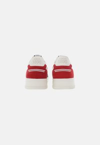 Zapatillas de ante rojas con suelas blancas, que presentan un pequeño logo "DESDE 1890" en el talón y costuras decorativas en los lados.