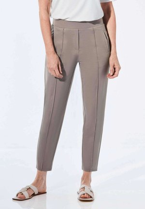 Pantalons gris ajustés à taille haute, avec deux poches avant et des détails de couture verticale ; portés avec des sandales à glissière de couleur claire.