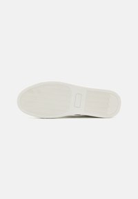 Fehér sneaker talp, texturált barázdákkal, sima felülettel és gumiból készült anyaggal. A márkajelzés a sarok területén látható.