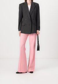 Czarna marynarka w paski w stylu double-breasted, dopasowane ramiona, zestawiona z różowymi spodniami w stylu dzwonów i czarnymi butami na obcasie, trzymając małą czarną torbę.