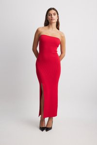 Rotes, geripptes, trägerloses Kleid mit figurbetontem Schnitt, das einen seitlichen Schlitz und ein knöchellanges Design aufweist, kombiniert mit schwarzen, spitzen Absatzschuhen.