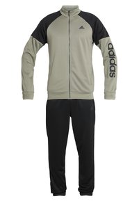 Veste zippée beige et noire Adidas avec logo sur la poitrine et la manche, associée à un pantalon noir Adidas avec un logo discret près de la poche.