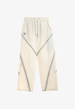 Pantalones de corte ancho color blanco roto con cintura elástica, cordón frontal, bolsillos laterales, rayas diagonales negras y pequeño logo circular en el muslo izquierdo.