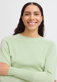 Maglione leggero verde chiaro con polsini a costine e collo rotondo. Tessuto morbido e design semplice, con maniche raglan.