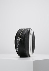 Borsa ovale in pelle nera con due cerniere laterali, caratterizzata da strisce verticali bianche. Superficie testurizzata con un accento del marchio. Design minimalista.