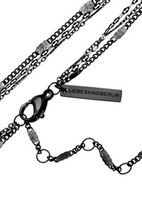 Svart metallkedja med flera strängar som har texturerade länkar, inklusive platta ovaler. Spänne med en märkesskylt: "LIEBESKINDBERLIN."
