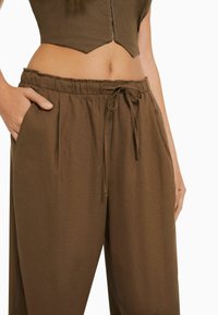 Pantalons bruns, l égers, à coupe décontractée, avec taille élastique, cordon de serrage et poches latérales, fabriqués à partir d'un tissu doux au toucher lisse.