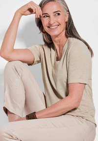 Helles beiges Kurzarmoberteil mit V-Ausschnitt, kombiniert mit figurbetonten, strukturierten beigen Hosen, die feine Muster und Akzente im Stoff aufweisen.