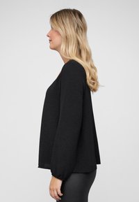Black long-sleeve top with a relaxed fit, textured fabric, and elasticized cuffs. The neckline is slightly scooped, and it drapes softly.
